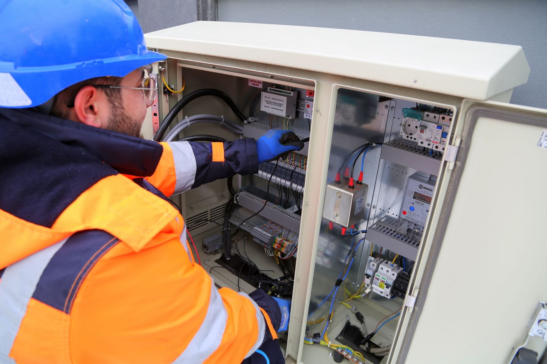 Engineer in safety gear working on an outdoor electrical panel.